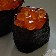 A plate of homemade sushi on a white stone kitchen counter, including salmon roe gunkan, ebi prawn nigiri and crab rolls.