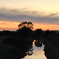 Sunset afterglow on the horizon, canal stretching away into the distance with a couple of trees and a solitary boat reflecting into it.