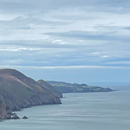 Rocks in the foreground with a view behind of grassy cliffs and the sea. Clouds in the sky