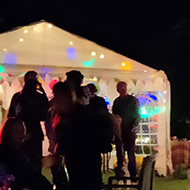 In pitch black night people are silhouetted against the colourful lights from party tents
