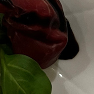 A bite-sized piece of smoked meat on a clean white plate. There is polished silver cutlery next to the plate.
