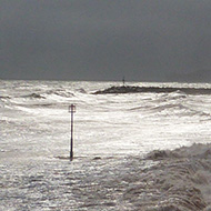 Waves breaking along the Sidmouth seafront, with dark clouds covering the sun and looming above the western horizon