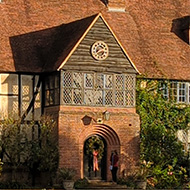 Photo of RHS Wisley late afternoon as the sun is setting lighting up The Laboratory building at RHS Wisley overlooking the ornamental pond which is reflecting the Arts and Craft style building