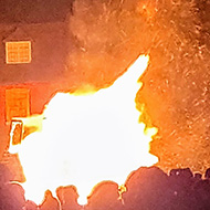 Picture of a bonfire in the left of the photo and windmill in orange in the background.