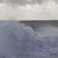 Big waves crashing into a pebbly beach throwing up large clouds of spray