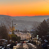 Looking down a steep icy street lined with houses towards a bright, multicoloured sunrise