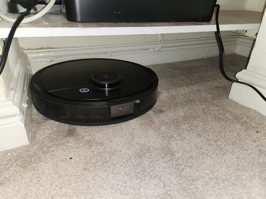 A close up of a robot vacum cleaner. A thick round black disk on wheels.