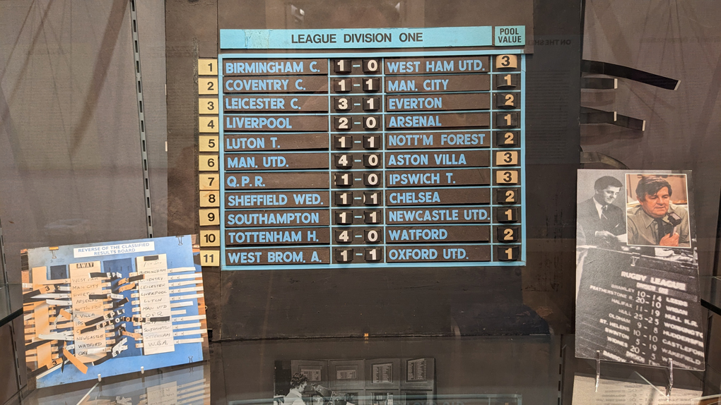 The day's football results, illustrated on a re-usable board where team-names are stuck-on and scores are illustrated thanks to pieces of tape with the numbers 1-9 on them and threaded through the board. A photograph in the corner of the image shows how the pieces of tape and are pulled through to display the correct score on-screen.