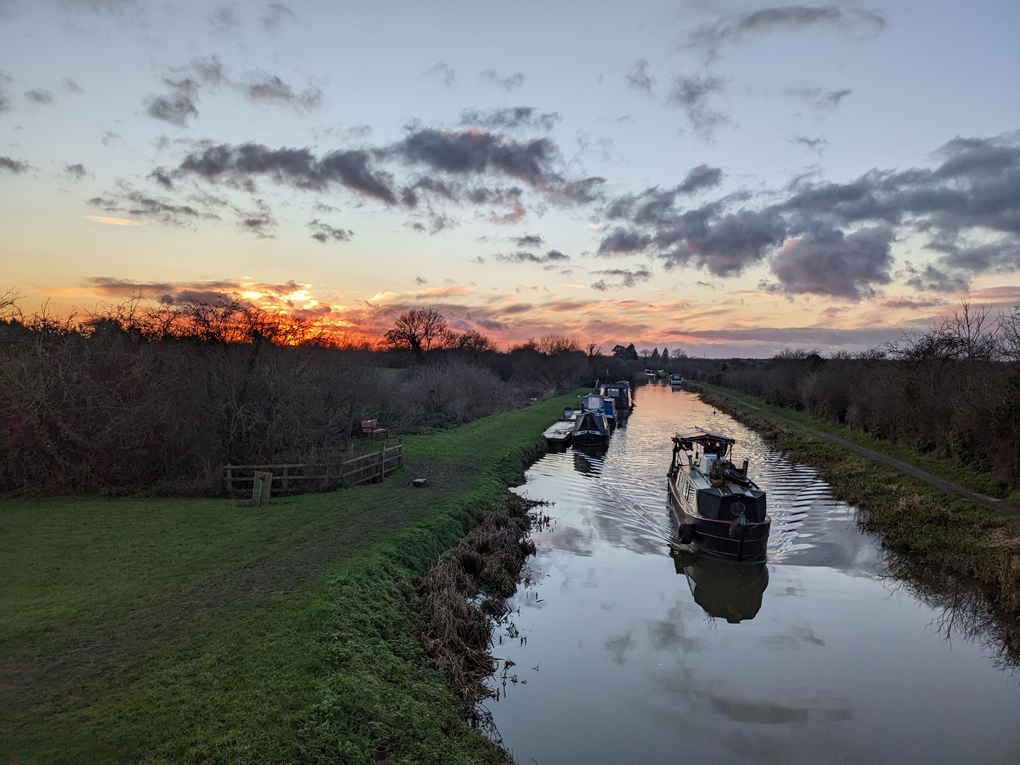 Sunset over a canal with a boat heading towards the bridge viewpoint