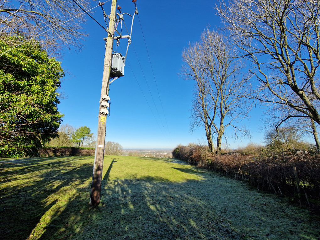 A wideangle view across a green field with a telegraph pole in the foreground, and clear, bright blue sky above