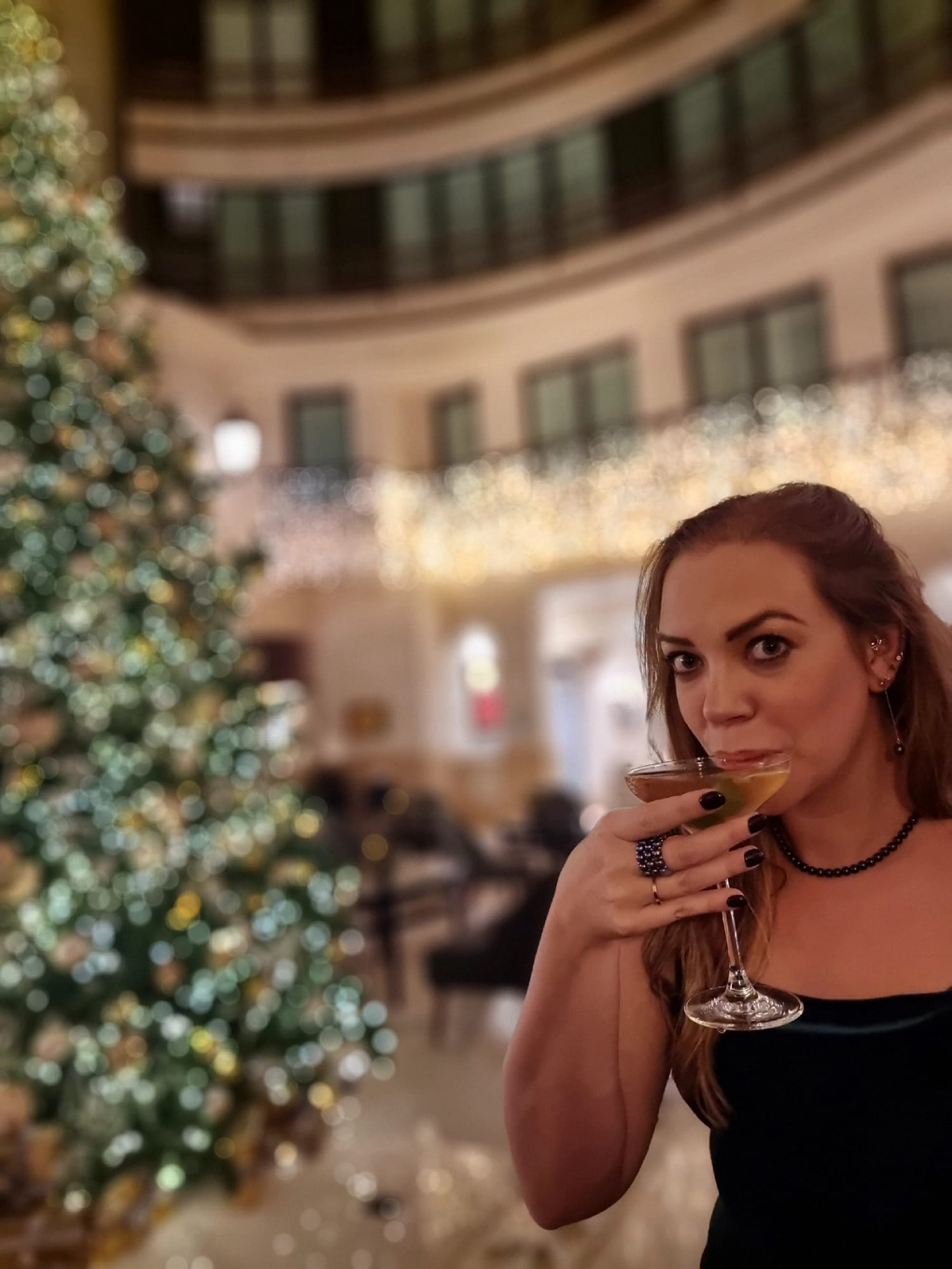 Lady drinking a martini in front of a big Christmas tree