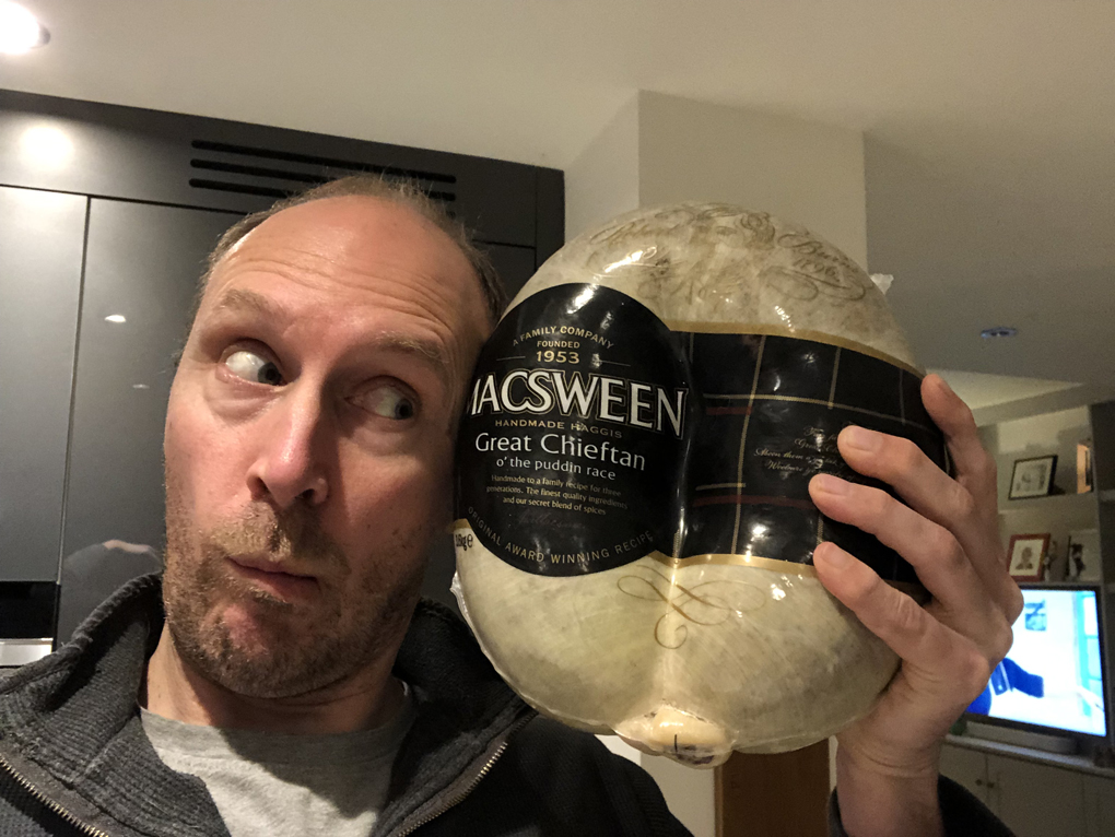 A fan with a strange look on his face holding up a haggis that is twice the side of his head.