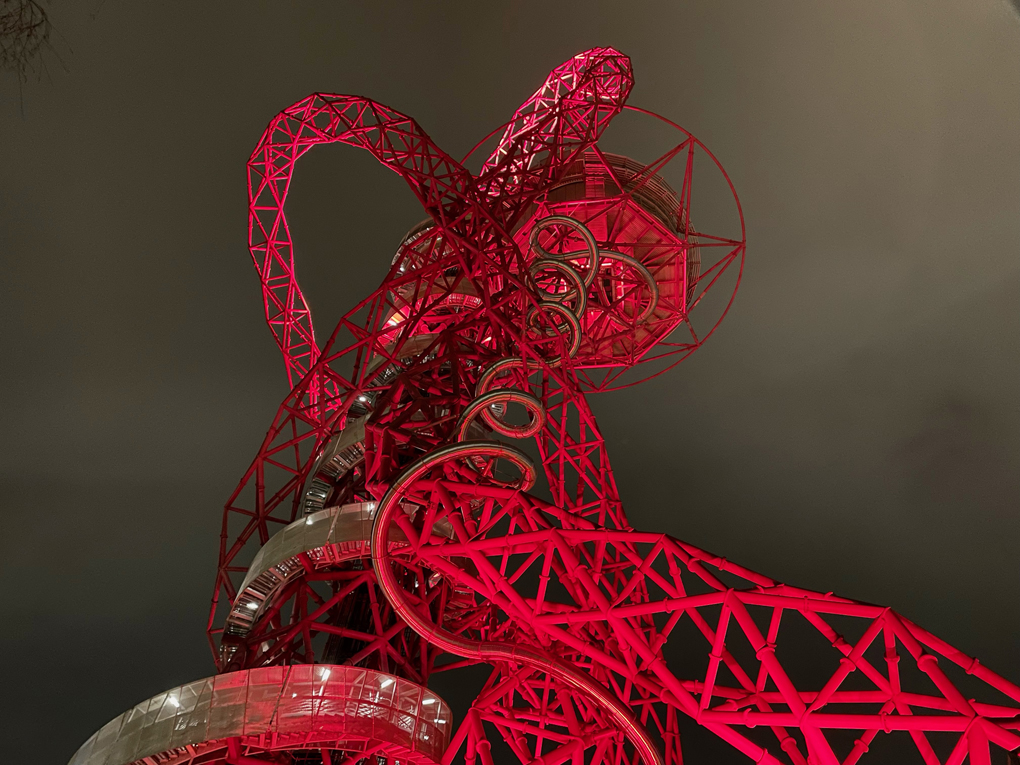 A tall metal structure from below. It's lit up red against a dark cloudy sky