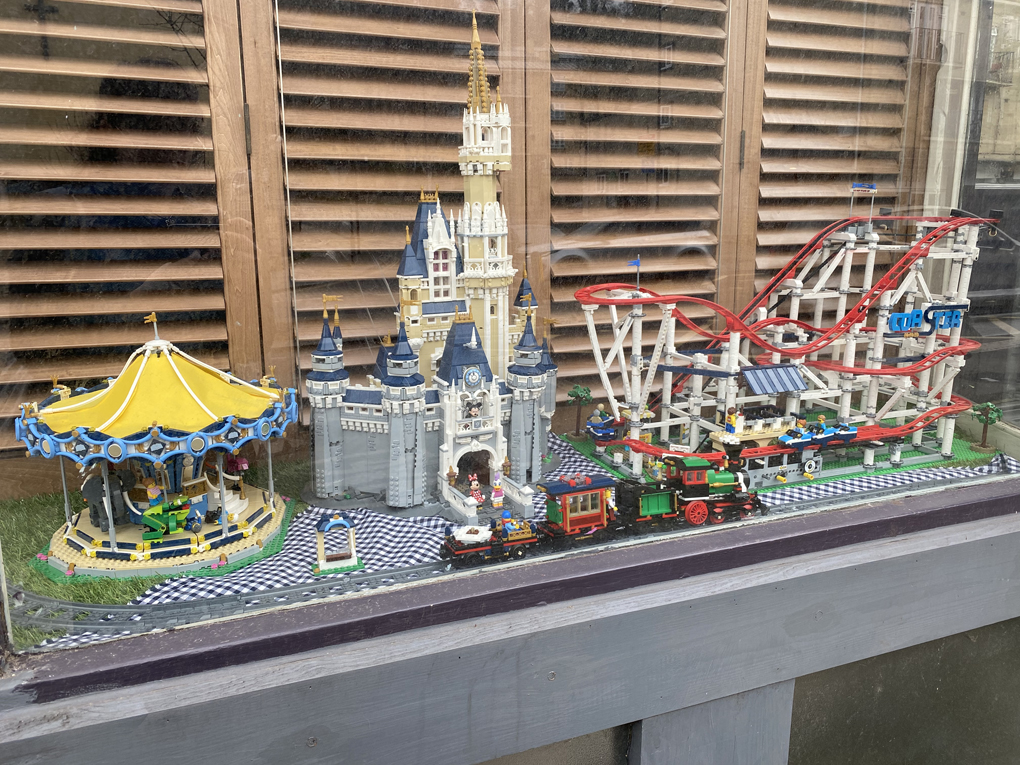A bay window at the front of a shop containing a Lego theme park. There is a carousel, a train, a rollercoaster and a castle with Mickey and Minnie Mouse on the balcony.