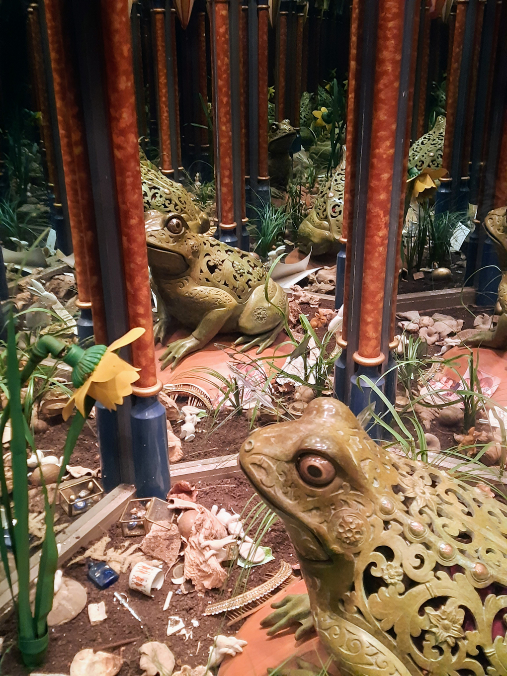 A large ornate frog figurine surrounded by plastic flowers and leaves. The edges of the picture are infinity mirrors giving the impression of the frog reflection going on forever.