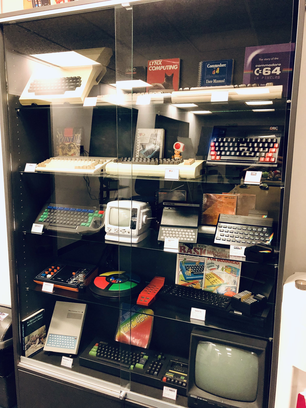 A display cabinet filled with computers from the 1980s, including various Spectrums, Commodores, Amstrads, and Amigas.