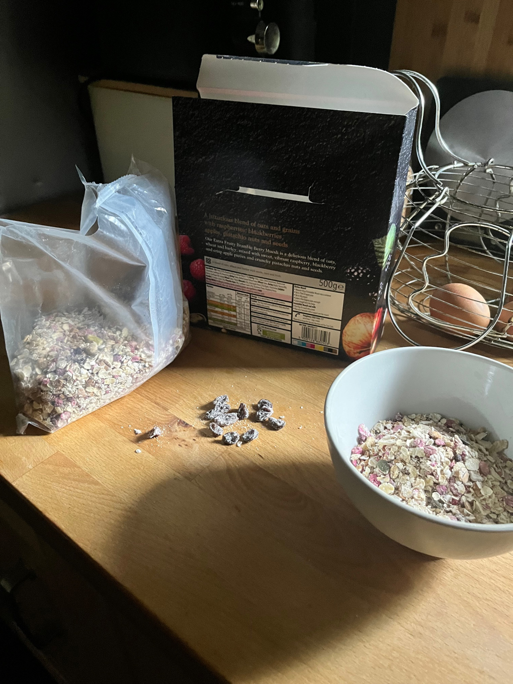 A bowl of muesli sat on a kitchen work surface. Next to the bowl are a handful of raisins that have been picked out and placed to one side.