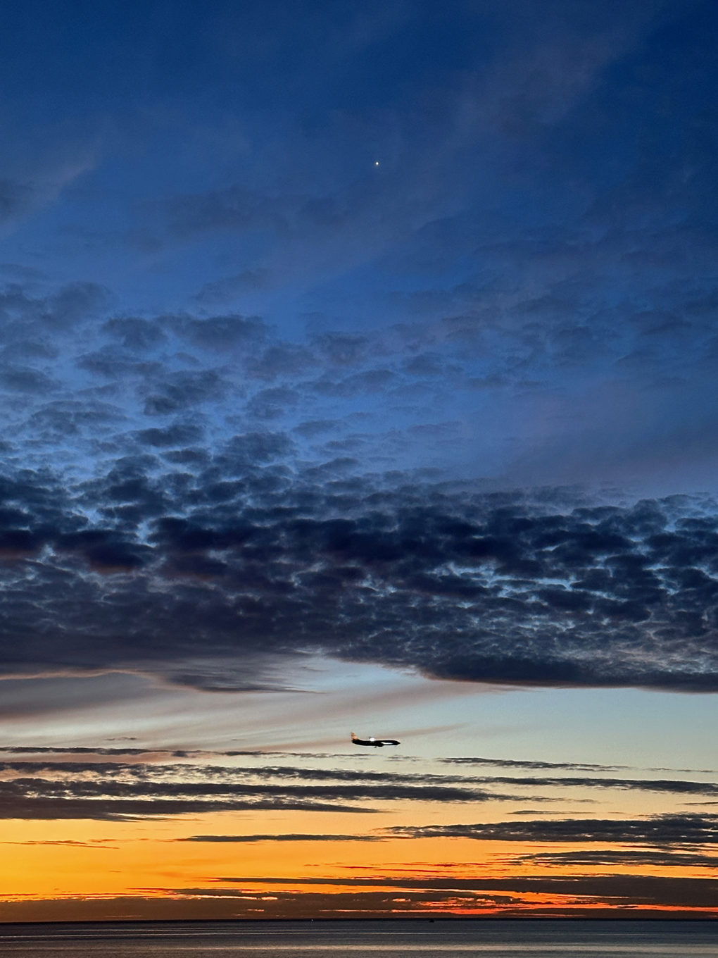 Sunset with dark cloud bands. Bright shining planet Venus top of frame and a plane flying across at the bottom.
