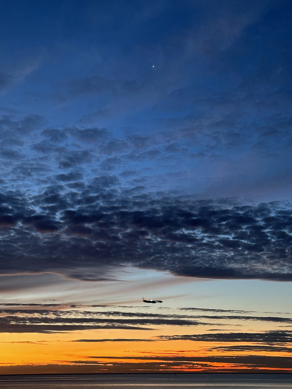 Sunset with dark cloud bands. Bright shining planet Venus top of frame and a plane flying across at the bottom.