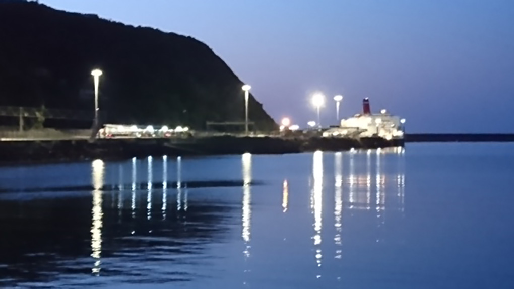 Fishguard Ferry having docked at dusk with all the lights on reflected on the sea with a promontory of land to its left. Next stop Ireland! An inviting sight in Goodwick harbour on a warm summer evening.
