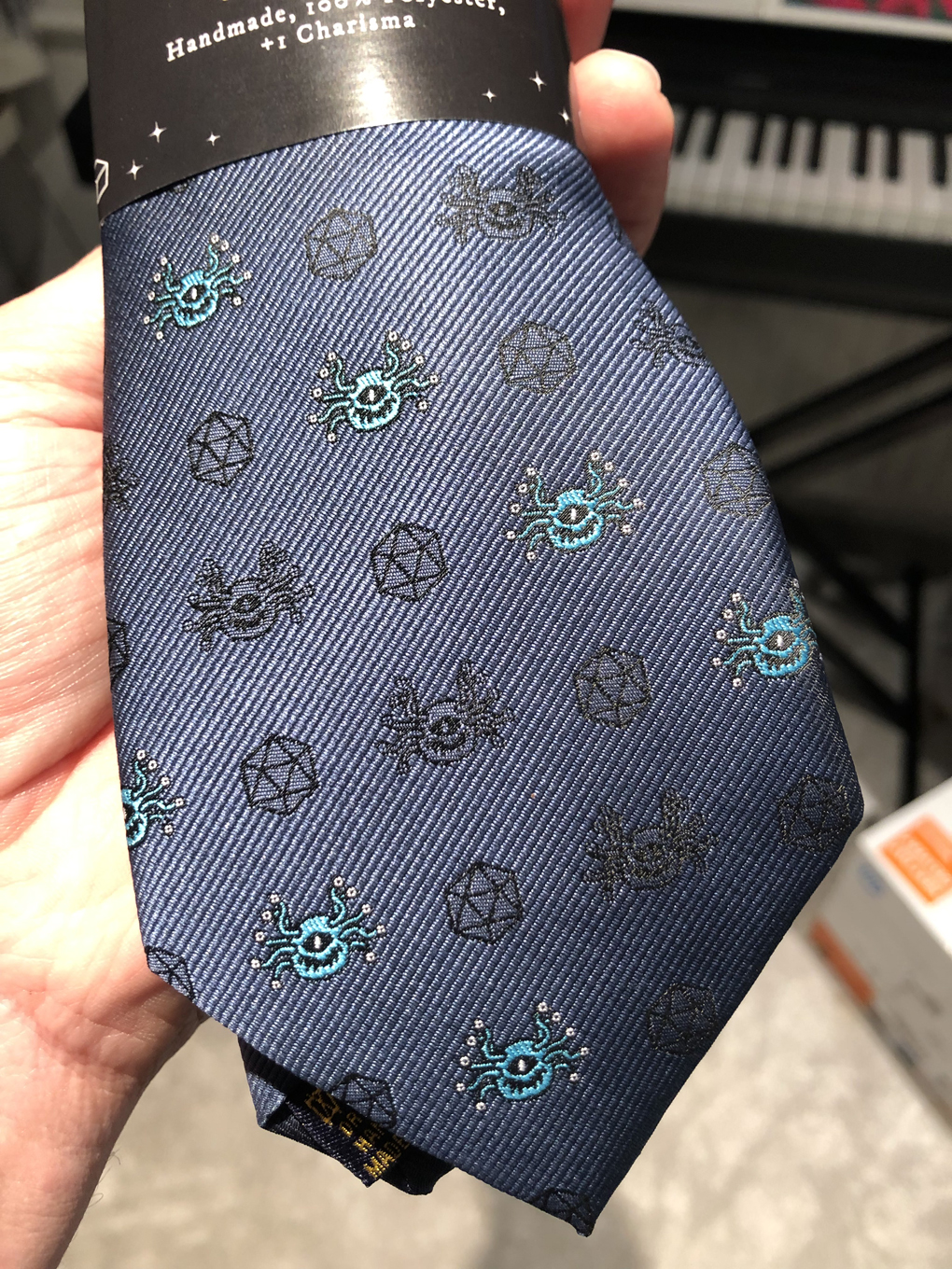 A blue tie with lots of tiny embroidered d20s and beholders