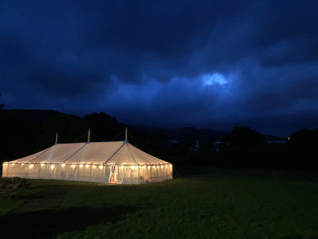 Picture of the glowing wedding marquee next to Derwentwater with storm clouds brewing above it.