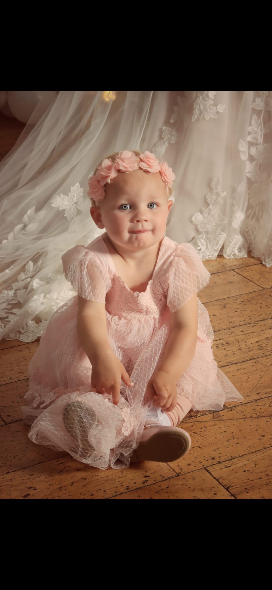 My granddaughter was a Flower Girl at her uncle’s wedding, she is sitting on the floor in a gorgeous pale pink dress, whilst sporting  a rather mischievous look on her pretty  face. The bride’s lace train  is the backdrop to the image.