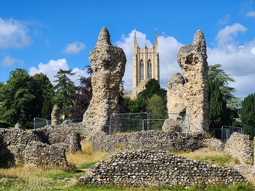 Ruins of the old Abbey. Two tall stone columns stand taller than the other ruins. They almost look like two rabbits standing on hind legs with their front paws clasped together in prayer. The Cathedral can be seen in the background between them.