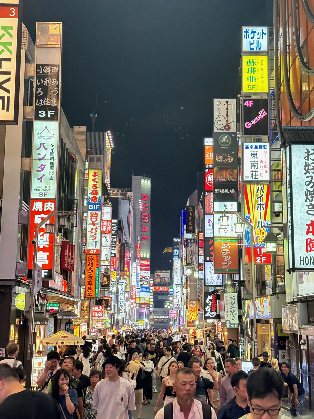 Tokyo street with many people and buildings with neon signs.