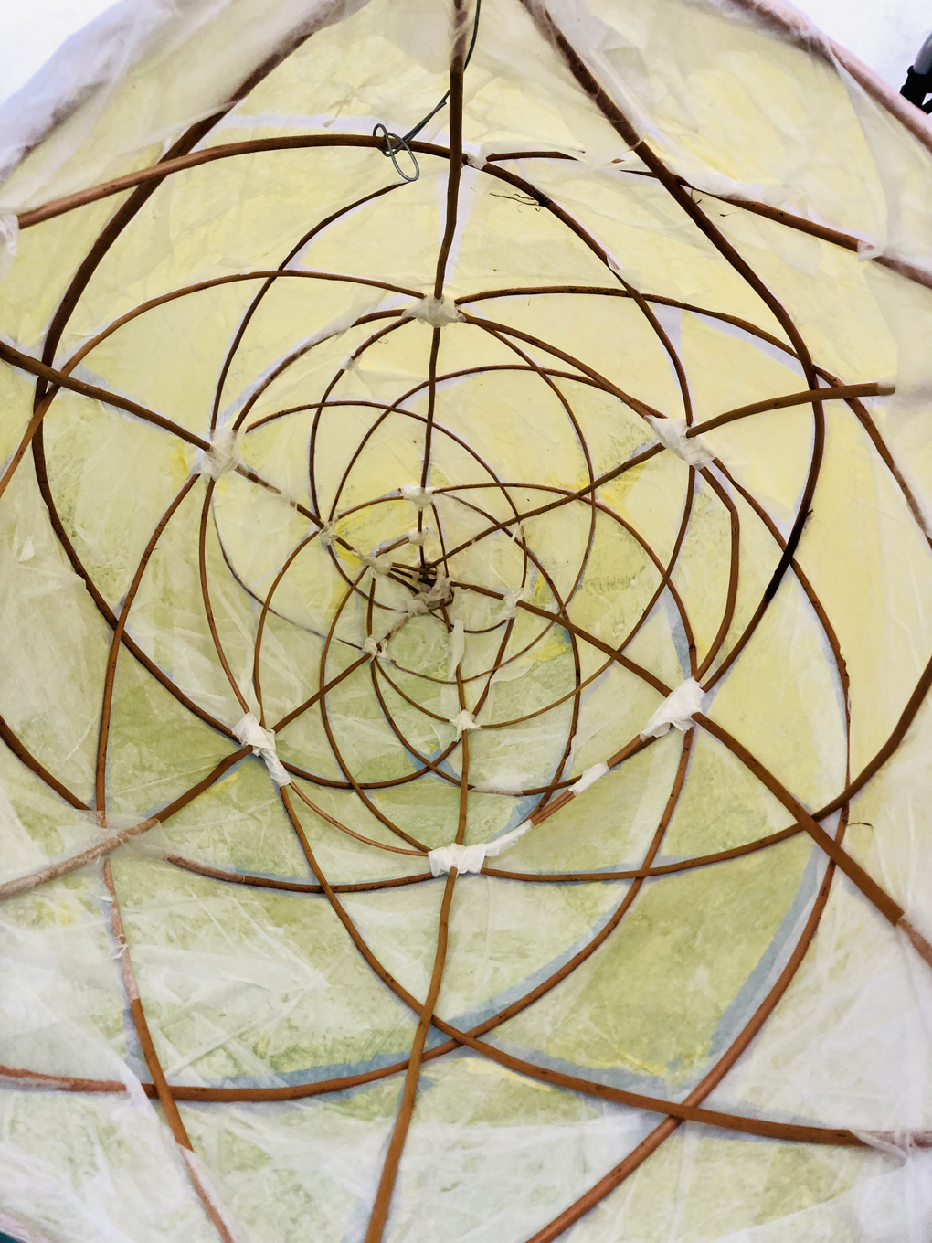 A geometric 3D sculpture of an ice cream cone, made from wicker, masking tape, and crepe paper, viewed from the inside.