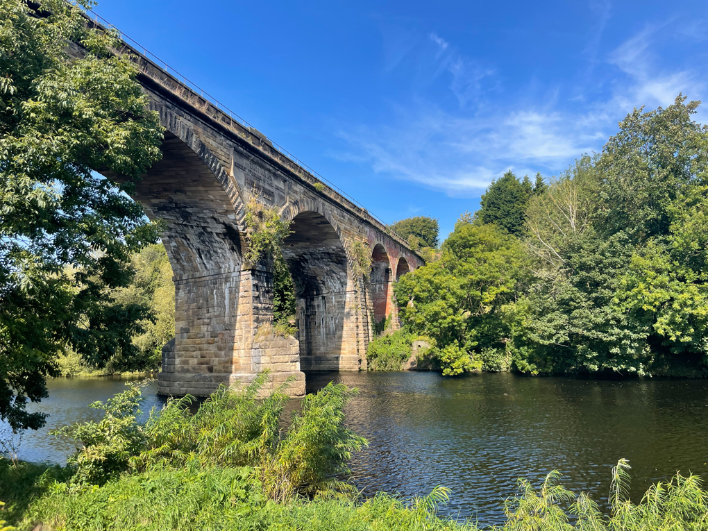 Large stone viaduct over river with trees in sunshine