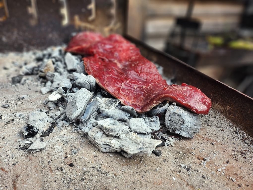 A rare beef flank lies on charcoal in a fire pit
