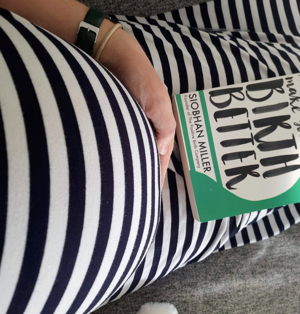 The bump of a heavily pregnant woman next to a book on hypnobirthing.