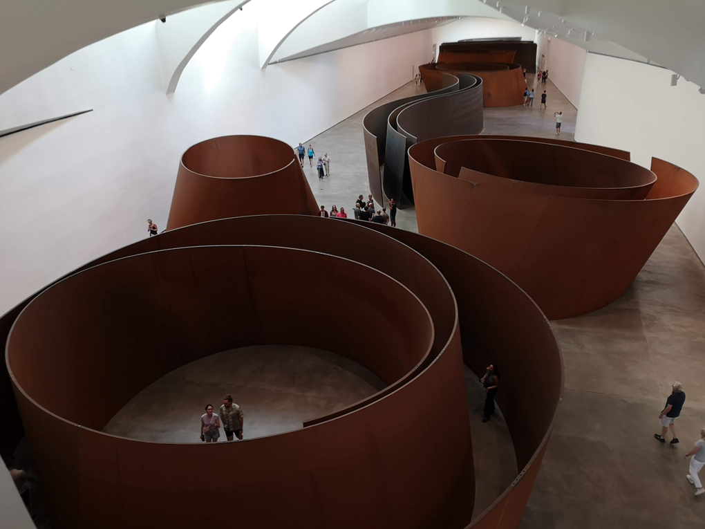 Large steel curved structures shown from above with people wandering amongst them.