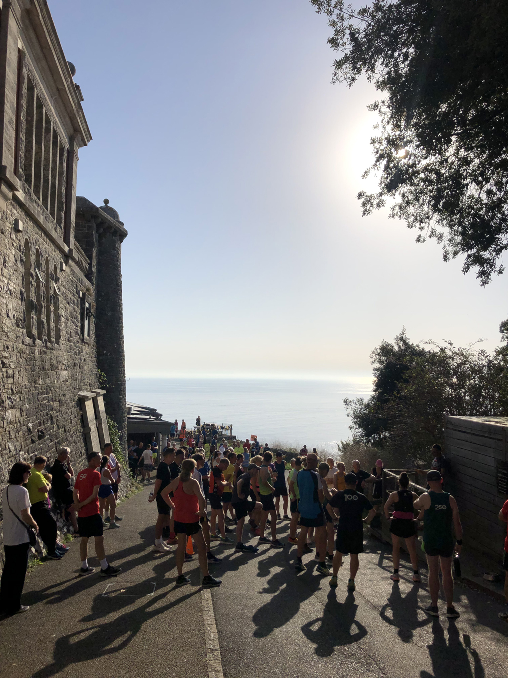 A crowd of people in running gear, with a stone fort on the left and the blue sky and sea extending to the horizon.