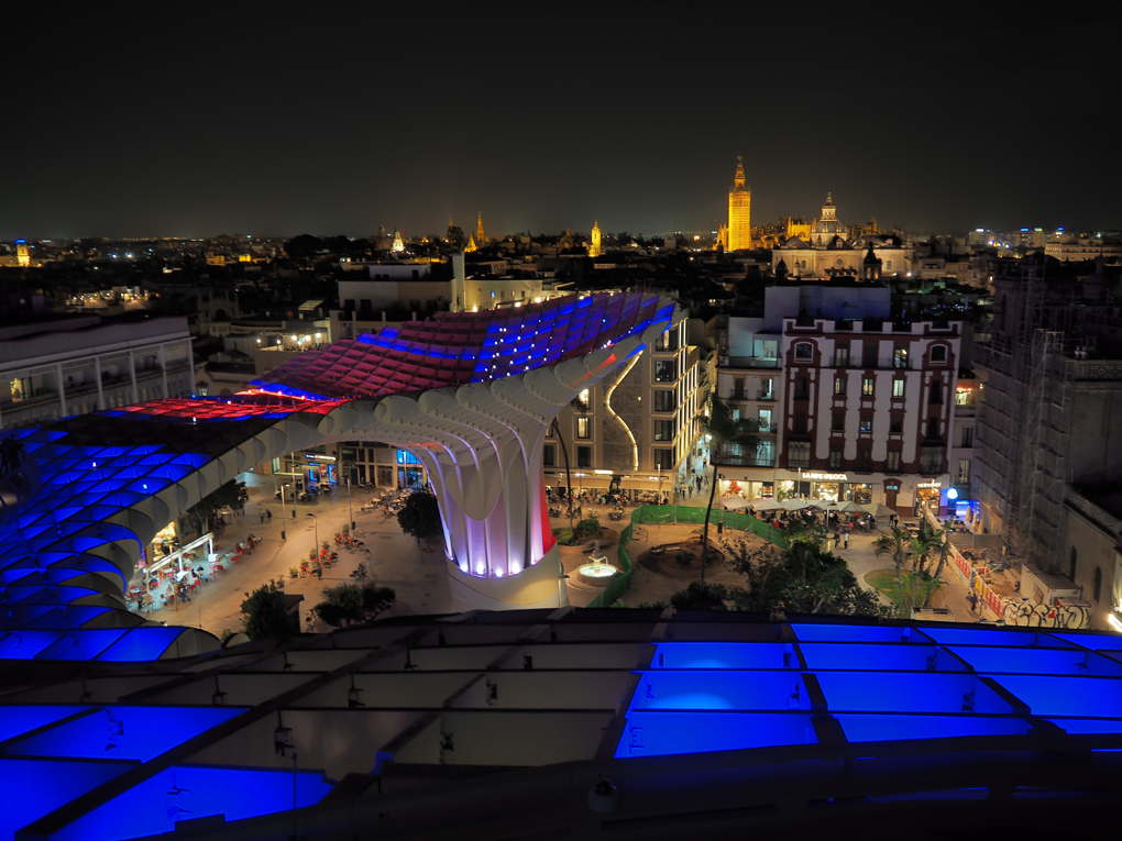 View from Las Setas in Seville at nighttime looking across the city, where the wooden strucutre of Las Setas itself is illuminated blue