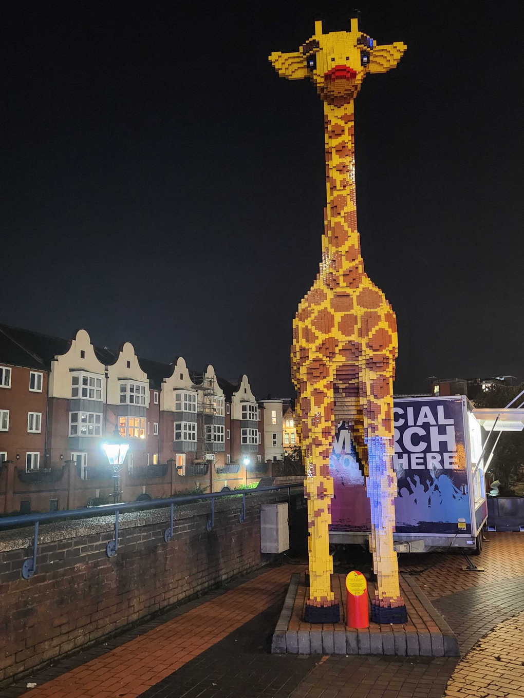 A life size giraffe made out of lego stands out against the night sky