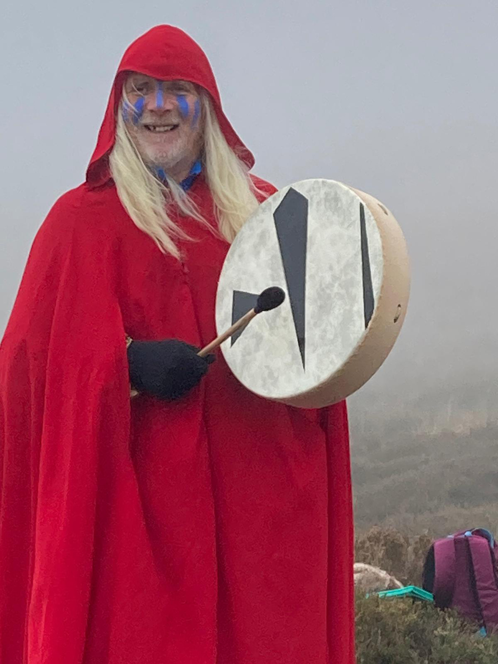 Man in red cloak with blue face paint and a hand drum