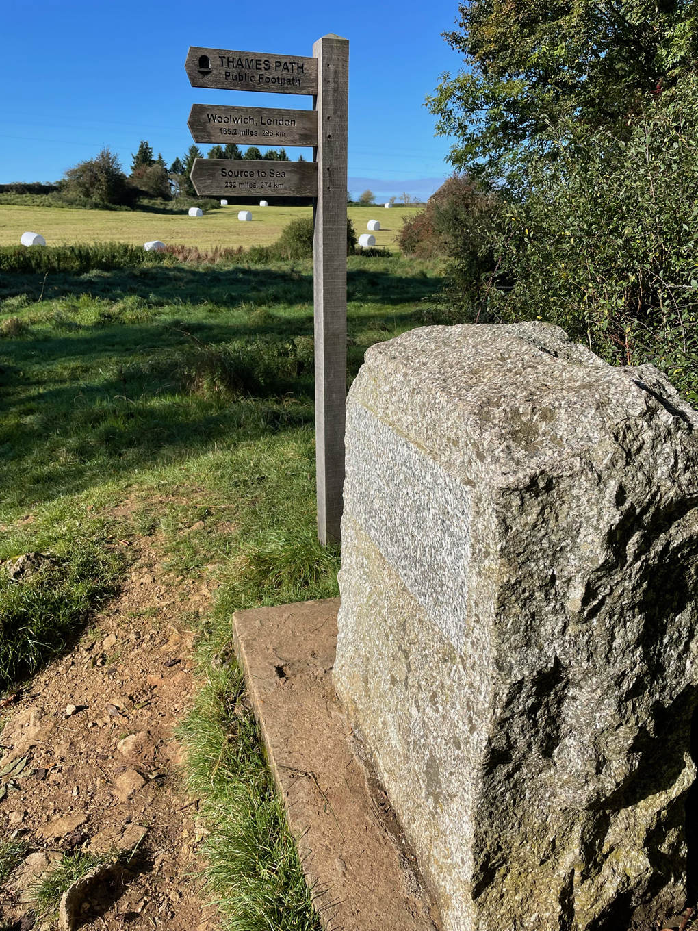 A wooden sign post in a field next to a plinth marking the source of the river thames