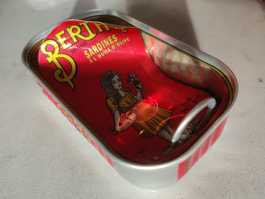a bright red Berthe brand sardine tin catches the lights with it's bright yellow typography and illustration of a flower girl