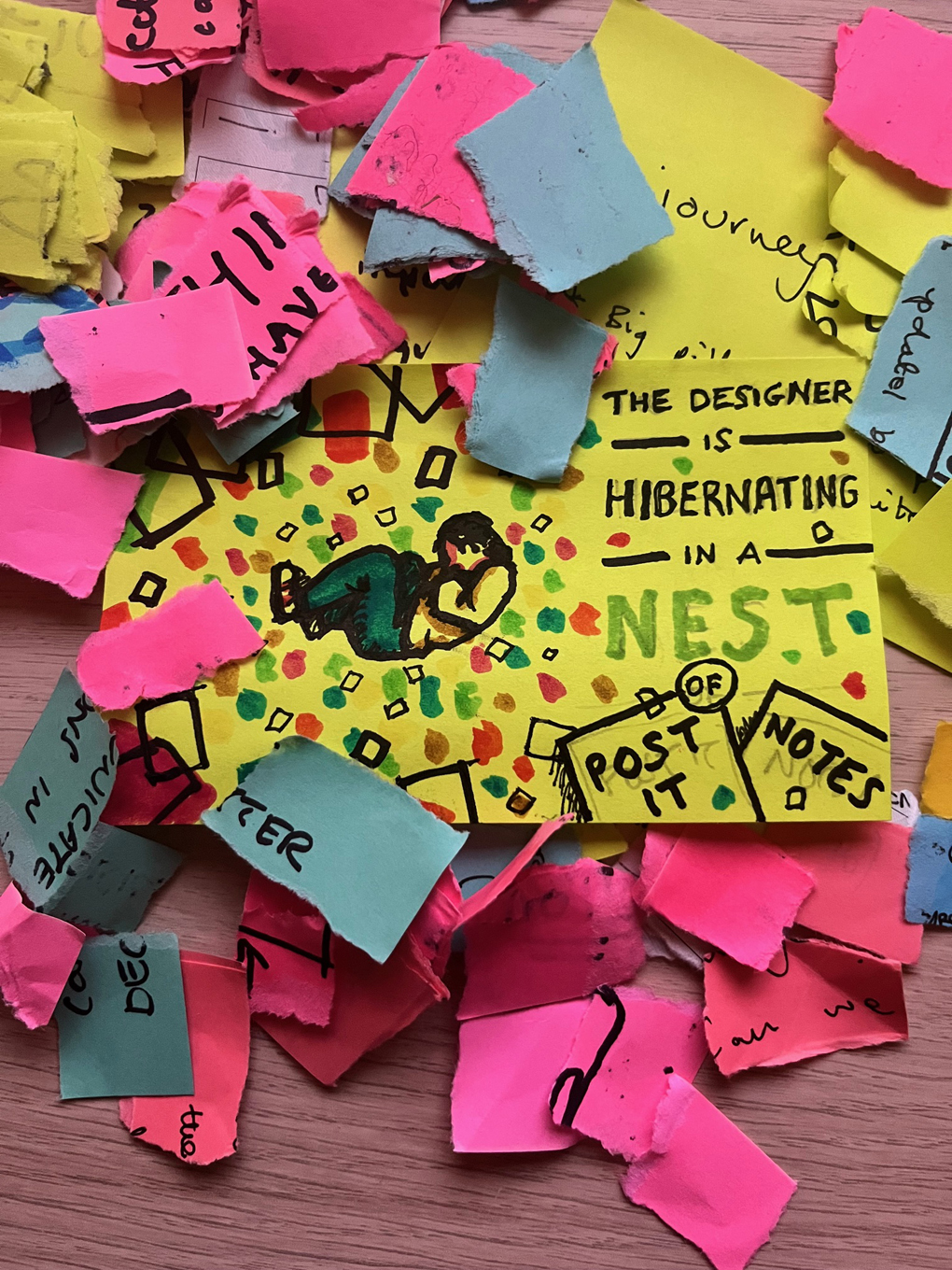 A pile of multi-coloured, torn-up post it note. In the middle of the pile is a drawing of a person curled up asleep. Next to the sleeping person there is text that reads “The designer is hibernating in a nest of post-it notes”