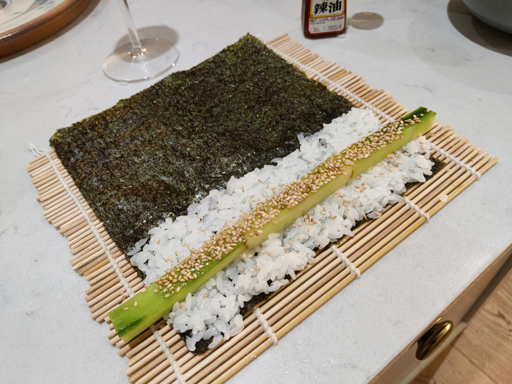 A half made cucumber hosomaki on a sushi rolling mat ready to be rolled.
