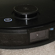 A close up of a robot vacum cleaner. A thick round black disk on wheels.