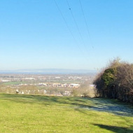 A wideangle view across a green field with a telegraph pole in the foreground, and clear, bright blue sky above