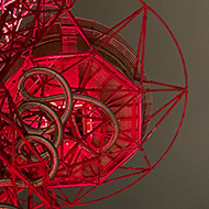 A tall metal structure from below. It's lit up red against a dark cloudy sky