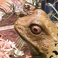 A large ornate frog figurine surrounded by plastic flowers and leaves. The edges of the picture are infinity mirrors giving the impression of the frog reflection going on forever.