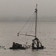 An old wooden boat sunk in the mud and an old tide marker are in the foreground, behind is the wide estuary of the River Exe shrouded in mist.