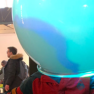 A young boy sitting on a chair in the Science Museum, with a big, opaque spherical helment over his head, emitting a soft blue glow.