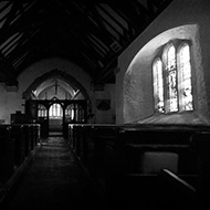 Old stone church with wooden features and light spilling through the side window.