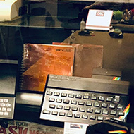 A display cabinet filled with computers from the 1980s, including various Spectrums, Commodores, Amstrads, and Amigas.